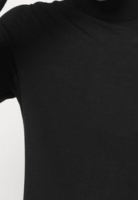 Maglione a collo alto nero con un design aderente, realizzato in morbido tessuto lavorato a maglia, caratterizzato da una texture liscia e una costruzione senza cuciture.