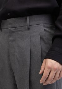 Grijze geplisseerde broek van een gestructureerde stof, met een vlakke voorkant en een vlakke tailleband, gecombineerd met een zwart shirt met lange mouwen.