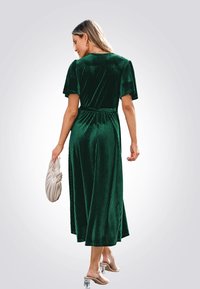 Abito in velluto a coste verde smeraldo, con maniche corte, vita stretta e gonna fluida. Abbinato a una pochette beige e tacchi trasparenti.