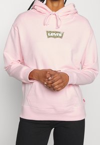 Felpa rosa realizzata in tessuto morbido, con tasca a marsupio, cappuccio regolabile e un logo Levi's leopardato sul petto.