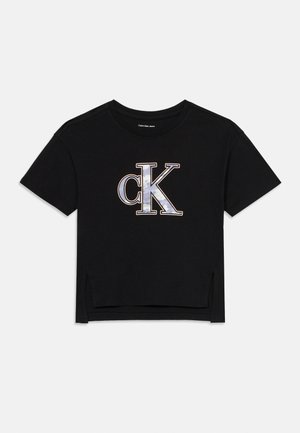 Černé zkrácené tričko vyrobené z bavlny, s velkým logem "ck" v šedé a bílé barvě s metalickými akcenty. Krátké rukávy, boční rozparky.