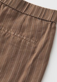 Brown fabric with thin white vertical pinstripes, featuring a stitched welt pocket and an elastic waistband.