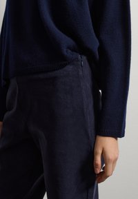 Pull en maille bleu marine avec un ourlet côtelé, associé à un pantalon en tissu lisse assorti. Comprend un détail de fermeture éclair sur le côté.