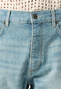 Jeans de mezclilla azul claro con un diseño clásico de cinco bolsillos, cierre de botón de metal y detalles de costura a lo largo de las costuras.