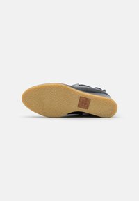 Chaussure en cuir noir avec une semelle en caoutchouc texturé de couleur tan. Présente un détail de logo sur la semelle et un design élégant.