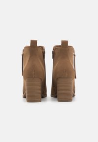Bottines en daim marron avec un talon carré, une fermeture éclair sur le côté et une languette à l'arrière. Talon texturé avec des rainures diagonales pour une meilleure adhérence.