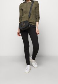 Olivgrön kabelstickad tröja, svarta slim-fit byxor, svart axelremsväska med gulddetaljer och vita sneakers med diskreta detaljer.