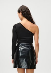 Fekete, egyvállas felső, redőzött kivitelben, fekete, fényes, műbőr miniszoknyával párosítva. Simább textúra és testhezálló sziluett.