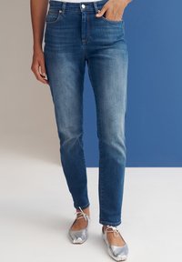 Fitted blue denim jeans with slight fading, five-pocket design, and visible stitching details, paired with silver ballet flats.