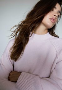 Lyserød strikket sweater med ribbet halsudskæring og manchetter. Blød tekstur, oversized pasform med raglanærmer. Enkel, minimalistisk design.