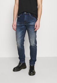 Jeans de denim azul oscuro con ligero desgastado, diseño ajustado, estilo de cinco bolsillos y un detalle de costura en contraste. Usados con botas negras.