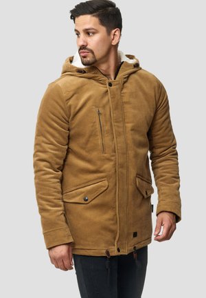 Hombre vestido con una chaqueta con capucha de pana color beige, con bolsillos de solapa abotonados y un bolsillo en el pecho con cremallera, mirando hacia un lado contra un fondo sencillo.