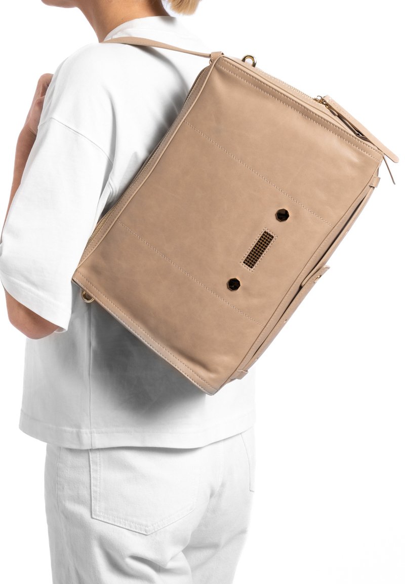 Tawny leren rugzak met een rechthoekige vorm, contrasterende textuur, een rits aan de voorkant en twee ronde hardwareaccenten op de achterkant.