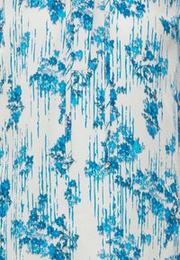 Tissu texturé avec un motif floral abstrait bleu et turquoise sur fond blanc, avec des cordons au niveau du décolleté.