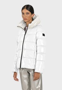 Witte pufferjas met een glanzende afwerking, capuchon en zwarte ritssluiting. Kenmerkt zich door horizontale stiksels en een logo patch op de linker mouw.