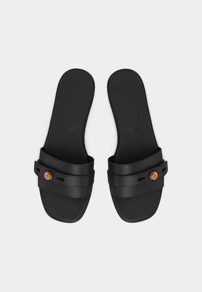 Μαύρα σανδάλια με ανοιχτά δάχτυλα τύπου slide με δύο οριζόντιες λουρίδες και έναν μικρό χρυσό κυκλικό έμβλημα σε κάθε λουρί, παρουσιάζονται πάνω σε λευκό φόντο.