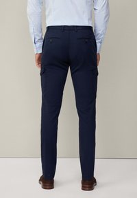 Marine cargobroek met zijzakken en een rechte pijpdesign, gemaakt van gladde stof. Gedragen met een lichtblauw gestreept shirt en bruine schoenen.