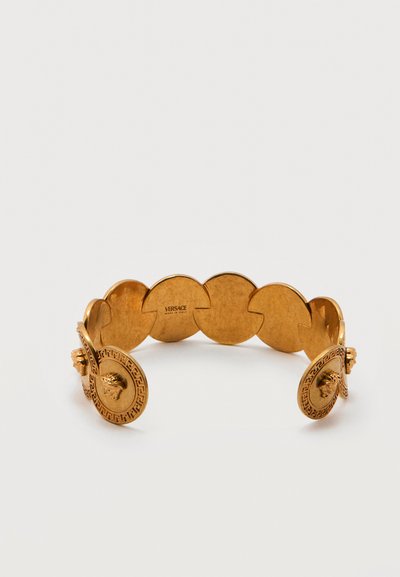 Βραχιόλι Versace σε χρυσό τόνο με συνδεδεμένα κυκλικά μετάλλια, διακοσμημένο με λεπτομέρειες κεφαλιού Μέδουσας και χαραγμένο το όνομα της μάρκας στο εσωτερικό.
