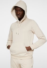 Felpa beige con cappuccio realizzata in tessuto morbido, dotata di tasca a marsupio, polsini a costine e un sottile logo sul petto.