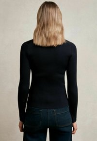 Fekete bordázott hosszú ujjú felső, testhez simuló fazonnal. A háta kerek nyakkivágású, sötét farmernadrággal párosítva.