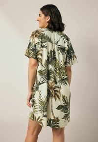 Tropenprint-Kleid mit kurzen Ärmeln, lockerer Passform und leichtem Leinenmaterial mit grünen Palmenblättern auf einem cremefarbenen Hintergrund.