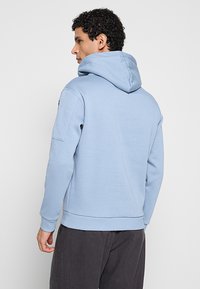 Lichtblauwe hoodie met een losse pasvorm, voorzien van een capuchon met trekkoord en geribbelde manchetten. Gemaakt van zacht materiaal, zonder zichtbare logo's of patronen.