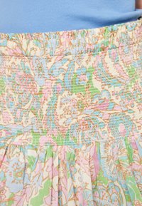 Jupe en tissu à motifs floraux avec une taille smockée. Les couleurs incluent le rose pastel, le bleu, le vert et le beige, avec des plis froncés à l'ourlet.