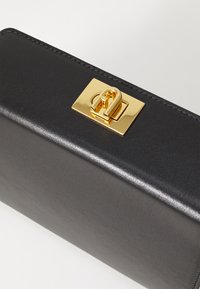 Zwarte lederen clutch met een glanzende gouden sluiting. Heeft een soepele textuur en nette stiksels langs de randen.