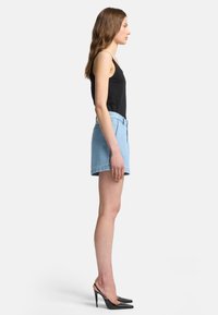 Shorts in denim chiaro con vita alta e orlo risvoltato, abbinati a una canotta nera e scarpe col tacco nere.