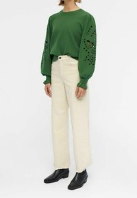 Sweat-shirt vert à manches bouffantes avec motifs floraux découpés, associé à un jean beige à jambes larges et des bottines noires.