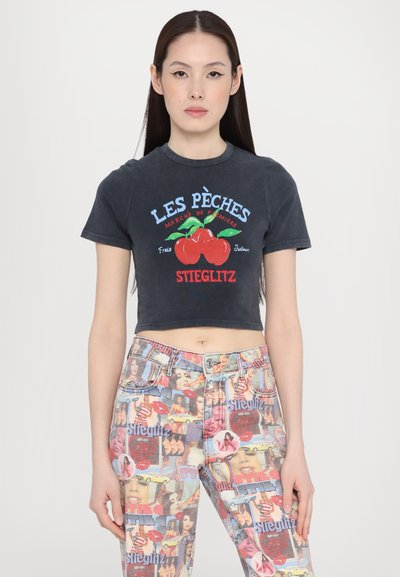 Black cropped t-shirt with graphic print featuring red cherries, green leaves, and text. Distressed denim pants with colorful collage pattern.