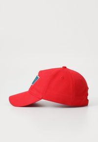 Rode katoenen pet met een gebogen rand, voorzien van een contrasterend blauw logo aan de zijkant. Het ontwerp bevat ventilatiegaten en een verstelbare strap.