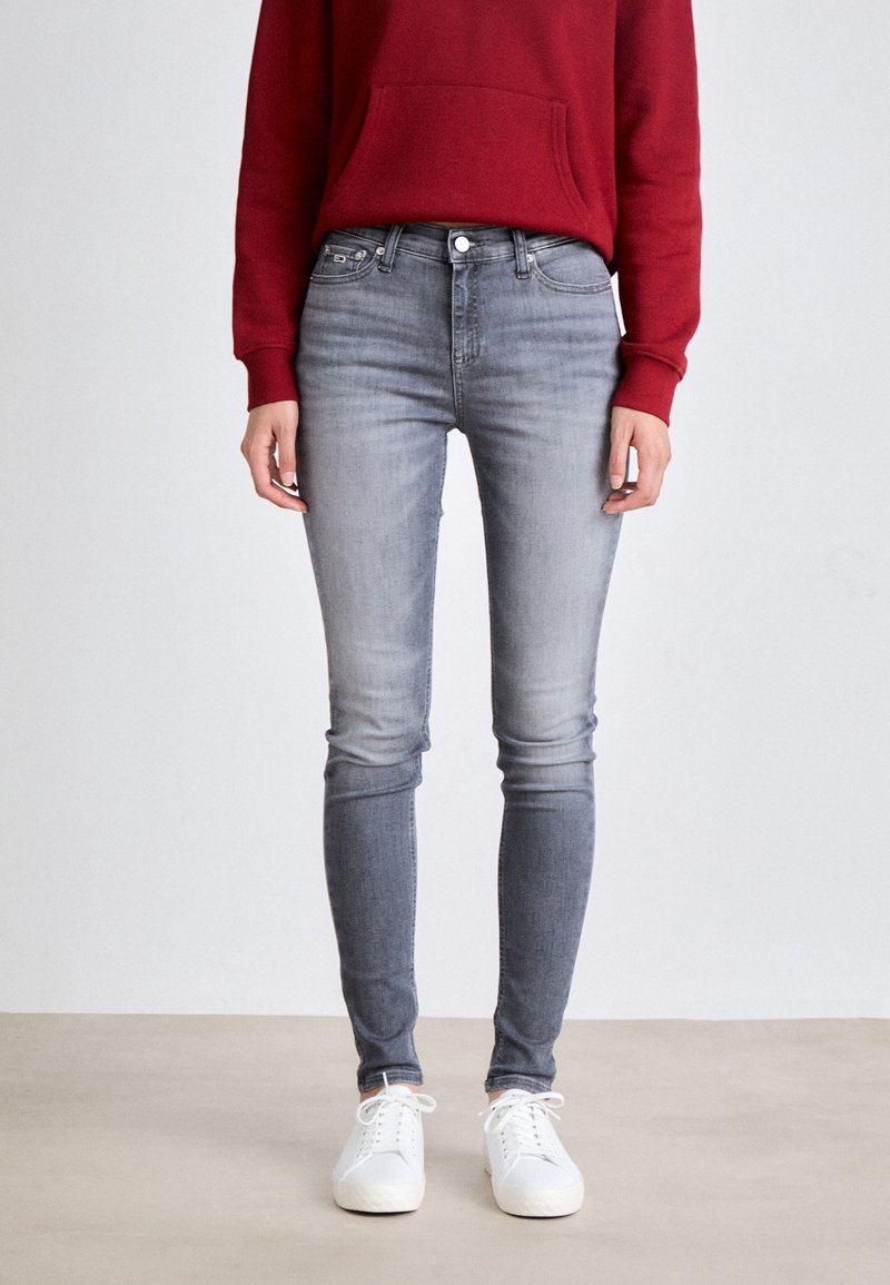 Jeans ajustados grises de mezclilla, con una cintura de altura media, cinco bolsillos y un acabado desgastado, combinados con zapatillas blancas y una sudadera roja.