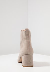 Botas de tobillo de ante beige con tacón cuadrado, que cuentan con una cremallera en el lateral y un acabado texturizado. Diseño simplista con punta redondeada.