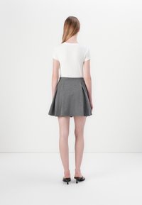 Haut blanc à manches courtes associé à une jupe plissée grise, présentant une texture lisse et une forme évasée, complétée par des sandales à talons noires.