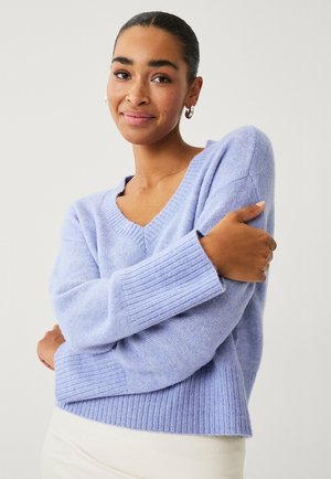 Pull à col en V lavande avec des poignets et un ourlet côtelés, fabriqué à partir d'un matériau doux, présentant une coupe décontractée et une surface texturée.