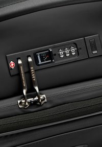 Bagages noirs avec une serrure TSA intégrée, dotés d'un clavier numérique, de doubles zips en métal et d'un petit port USB pour recharger des appareils.