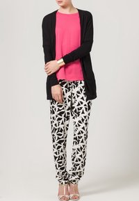 Czarny kardigan z długim rękawem na różowym topie, zestawiony z czarno-białymi spodniami w gwiazdkowe wzory oraz srebrnymi sandałami na obcasie.
