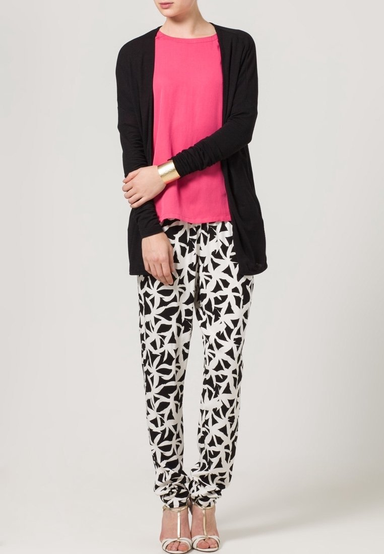 Czarny kardigan z długim rękawem na różowym topie, zestawiony z czarno-białymi spodniami w gwiazdkowe wzory oraz srebrnymi sandałami na obcasie.