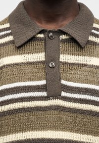 Πουλόβερ πόλο πλεκτό σε ελαιί πράσινο χρώμα με οριζόντιες ρίγες σε λευκό και καφέ. Διαθέτει γιακά, δύο κουμπιά και υφή στο ύφασμα.