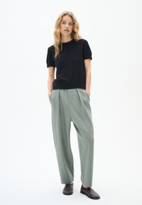 Top corto nero a maniche corte e pantaloni larghi di colore verde chiaro. Tessuto morbido, vestibilità rilassata, tasche laterali sui pantaloni e scarpe nere piatte.