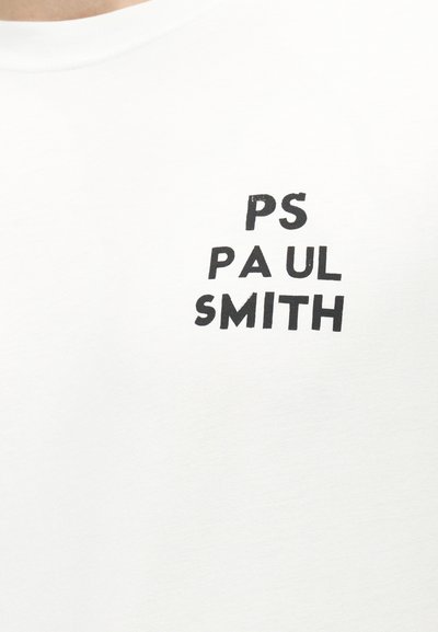 Λευκό πουκάμισο με μαύρο κείμενο "PS PAUL SMITH" τοποθετημένο σε στοίβα και ελαφρώς μετατοπισμένη διάταξη στην περιοχή του στήθους.