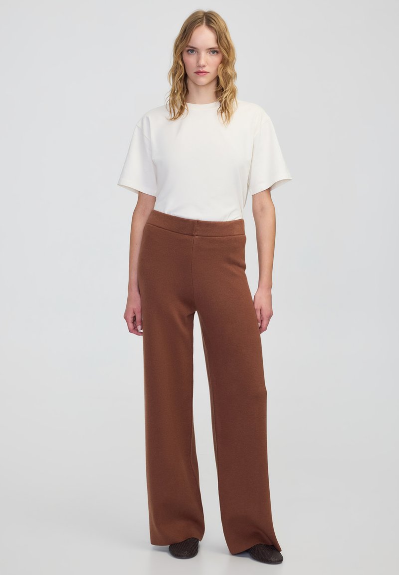 Witte korte mouwen shirt gecombineerd met hoge taille, brede bruine broek, met een gladde textuur en een elastische tailleband.