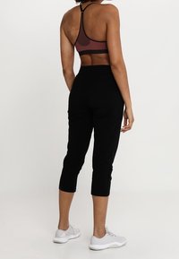 Svarta sportcapri-byxor med elastisk midja, i kombination med en röd och svart sport-bh med band. Grå sneakers fulländar looken.