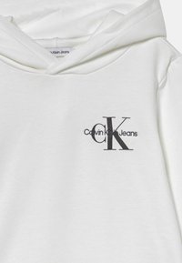 Bijela dukserica od mekanog materijala, sa prednjim džepom, kapuljačom s dricom i crnim izvezenim logotipom "Calvin Klein Jeans" na prsima.