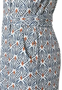 Weißer Stoff mit einem geometrischen Muster in Blau und Rost, mit betontem Taillenschnitt und seitlichen Taschen, der eine glatte Textur und ein strukturiertes Design zeigt.