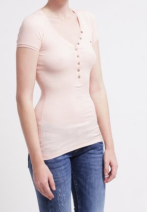 Top ajustado de manga corta color rosa claro con cuello en V, que presenta una botonera y textura acanalada. Combinado con jeans de mezclilla.