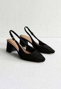 Tacchi slingback in suede neri con punta affusolata e tacco a blocco quadrato. Dotati di una tracolla regolabile con fibbia dorata.