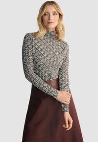 Czarna bluzka z długim rękawem i golfem w geometryczny biało-czarny wzór, w połączeniu z burgundową spódnicą; dopasowany krój z gładką teksturą.