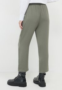 Pantalons légers et texturés de couleur vert olive avec une taille élastique, associés à des bottes noires à lacets avec une semelle épaisse.
